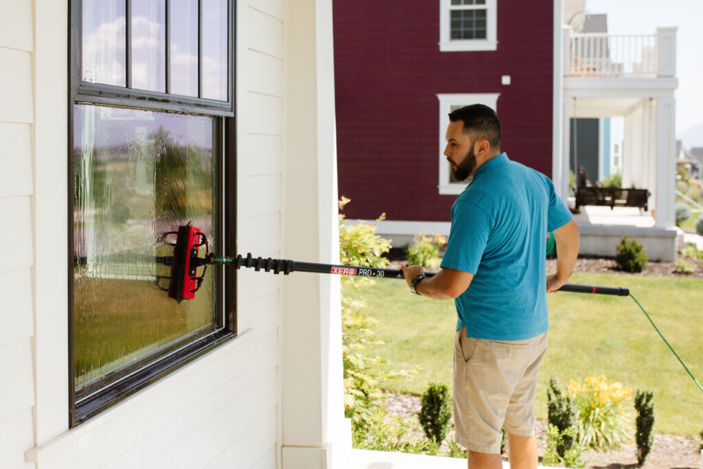 Technician performing residential window cleaning using a water-fed pole system in a modern suburban Utah neighborhood.